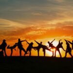 Group of people silhouetted against a vibrant sunset, showcasing unity and joy.