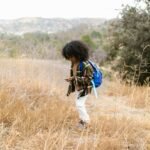 A young boy in a plaid shirt explores a dry field, surrounded by nature.