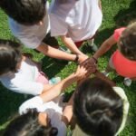 Top-view of children joining hands as a team in a sunny park, promoting unity.